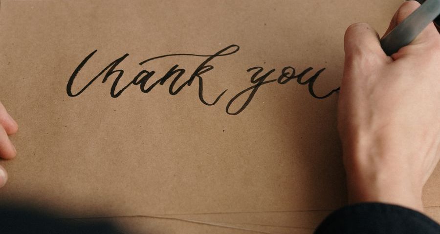 A hand writing thank you in black on a brown envelope by cottonbro from Pexels