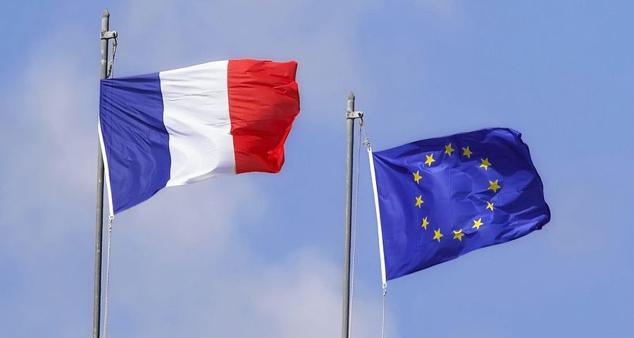 The French & EU flags flying next to each other against a blue sky