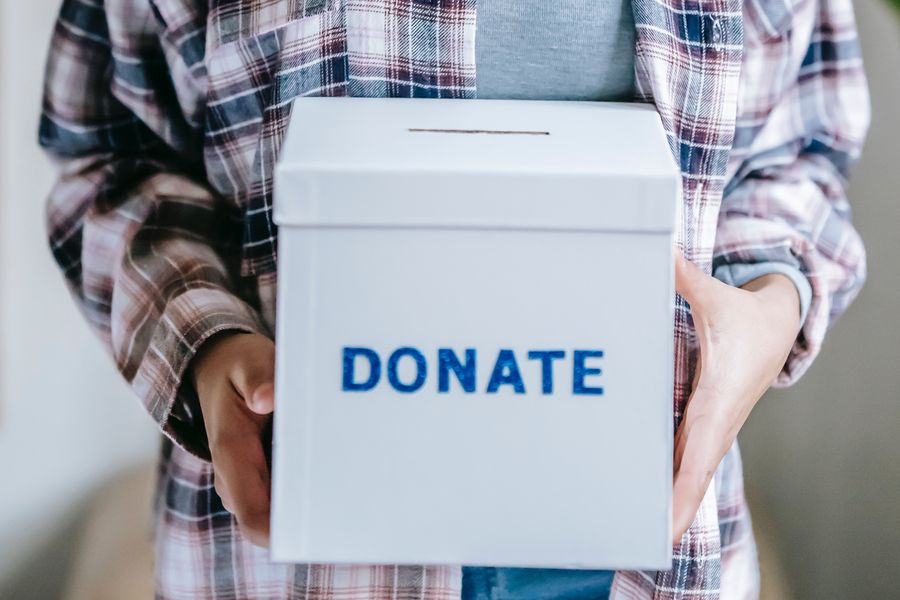 A woman's hands hold a white box with the word Donate on it in blue. By Liza Summer on Pexels