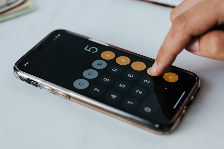 A finger presses the plus key on a smartphone calculator. By Karolina Grabowska on Pexels