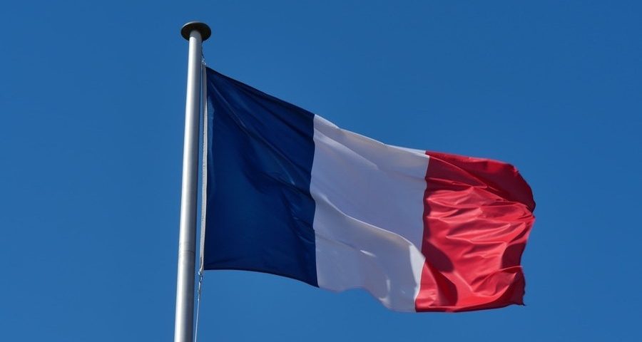 The French flag flies against a clear blue sky. By Rafael Garcin on Unsplash