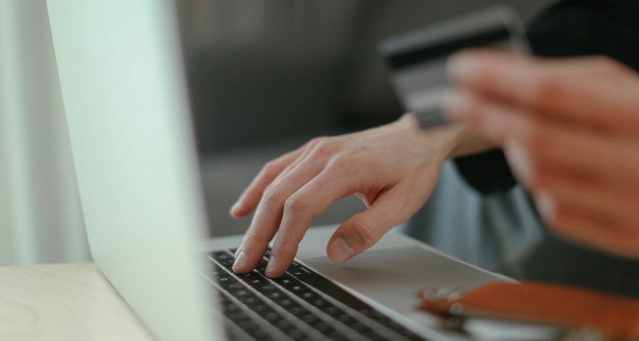 A hand on a laptop keyboard while the other hand holds a credit card. By Cup of Couple on Pexels