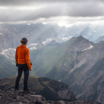 A climber stands at the top of a mountain, looking out at the view of other mountains. By Marek Piwnicki on Pexels.