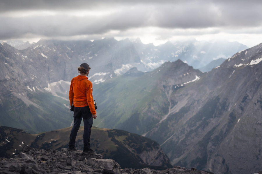 A climber stands at the top of a mountain, looking out at the view of other mountains. By Marek Piwnicki on Pexels.