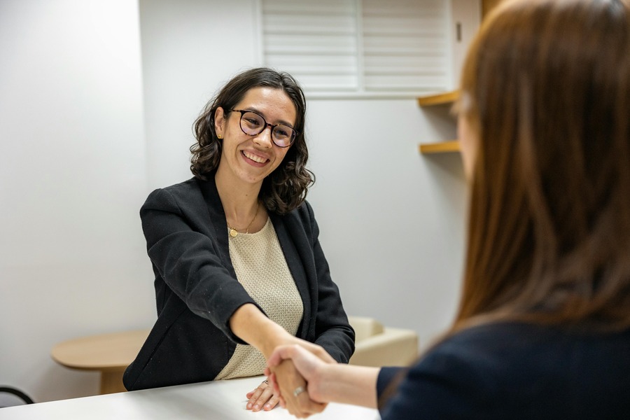 Two women shake hands across a desk in an interview. By Resume Genius on pexels