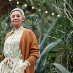 An over-50s woman with short grey hair looks at the camera, against a background of greenery. By Marcus Aurelius on Unsplash