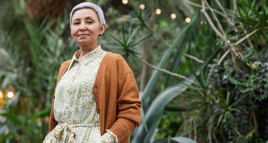 An over-50s woman with short grey hair looks at the camera, against a background of greenery. By Marcus Aurelius on Unsplash