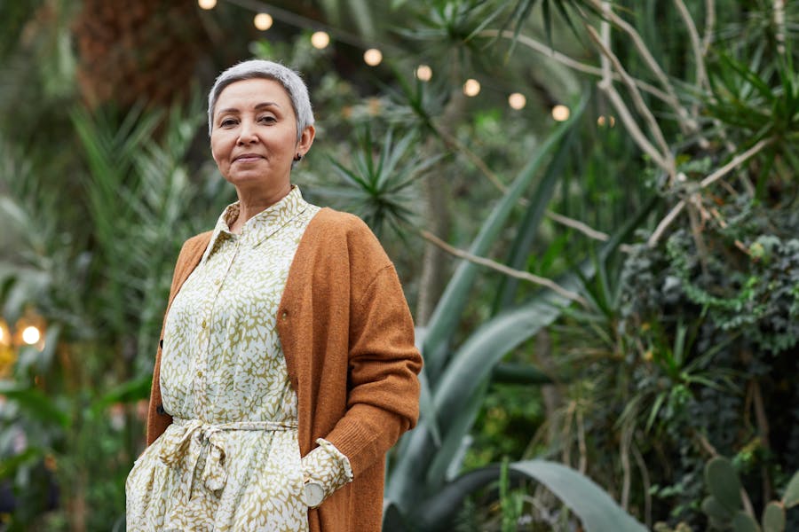 An over-50s woman with short grey hair looks at the camera, against a background of greenery. By Marcus Aurelius on Unsplash