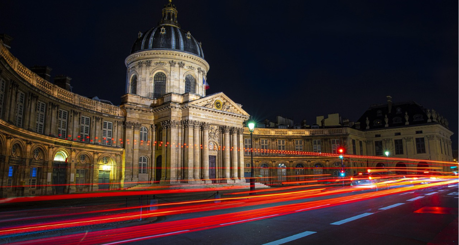 Red lights speeding past a historic building.By Céline Martin from Pixabay