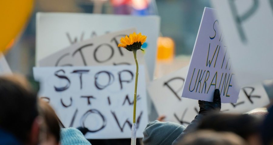 People hold up protest signs and a sunflower in a demonstration again Russia's invasion of Ukraine. By Derek French on Pexels