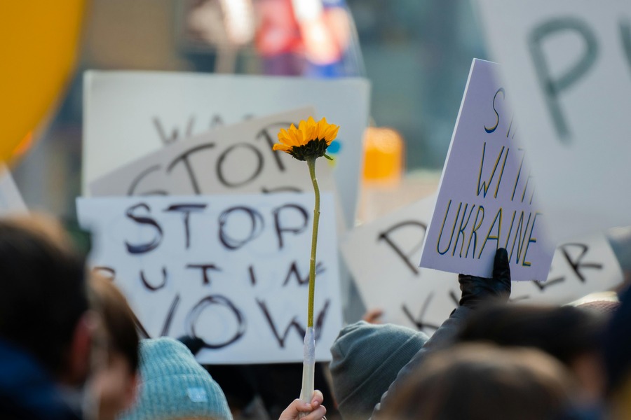 People hold up protest signs and a sunflower in a demonstration again Russia's invasion of Ukraine. By Derek French on Pexels