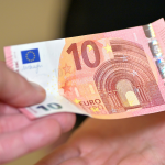 A hand giving a 10 euro note to another person. By Andres Siimon on unsplash