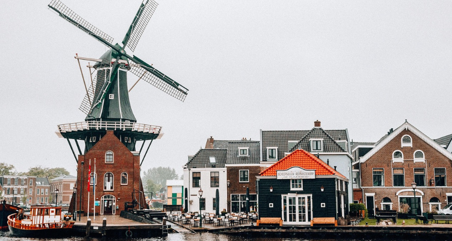 A picture of a windmill next to water, by Helena Jankovičová Kováčová from Pixabay