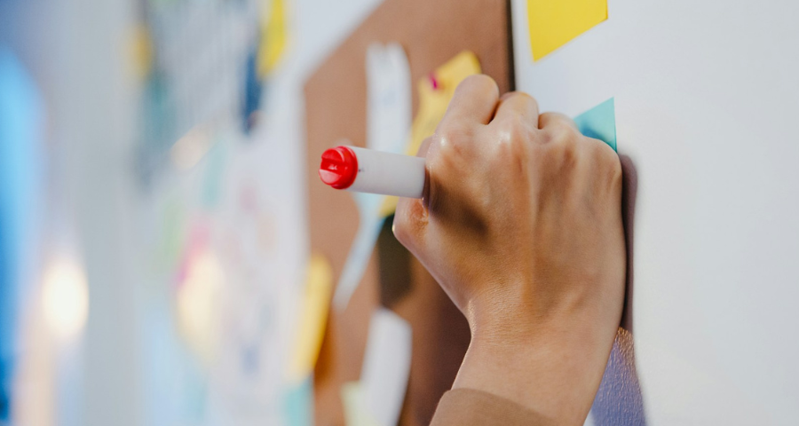 A woman's hand writing on a post-it note on a board. By Getty Images for Unsplash+