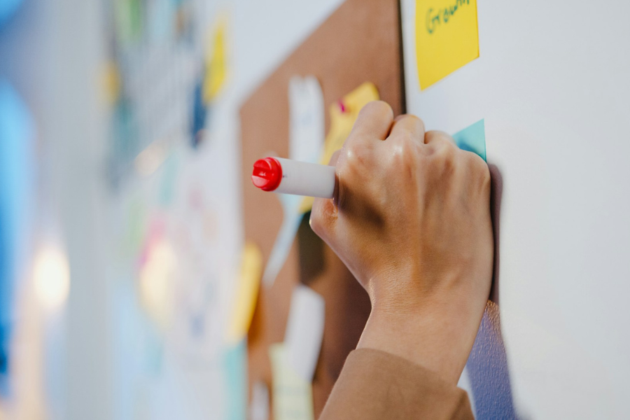 A woman's hand writing on a post-it note on a board. By Getty Images for Unsplash+
