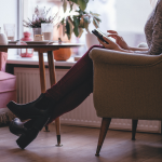 A woman sitting by a small table, uses her phone. By freestocks photos on Pixabay