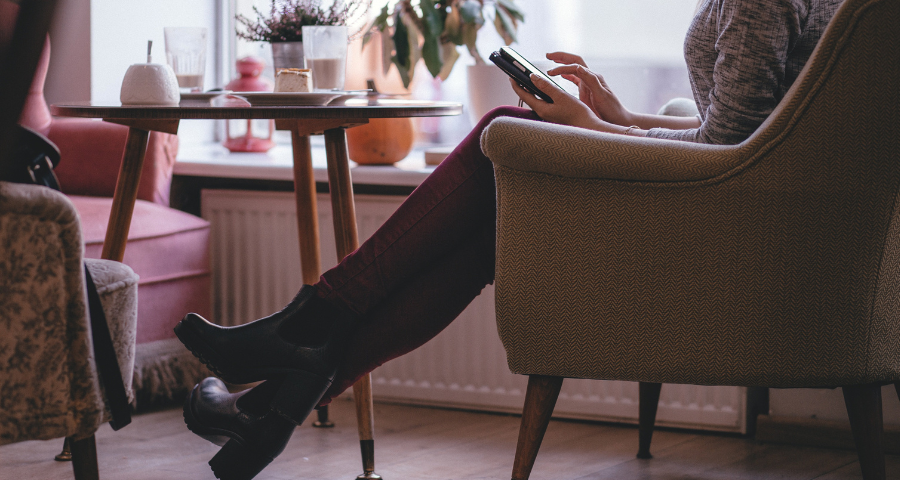 A woman sitting by a small table, uses her phone. By freestocks photos on Pixabay