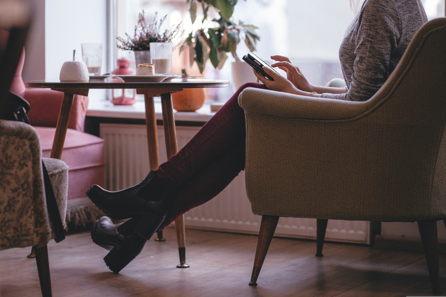 A woman sitting by a small table, uses her phone. By freestocks photos on Pixabay
