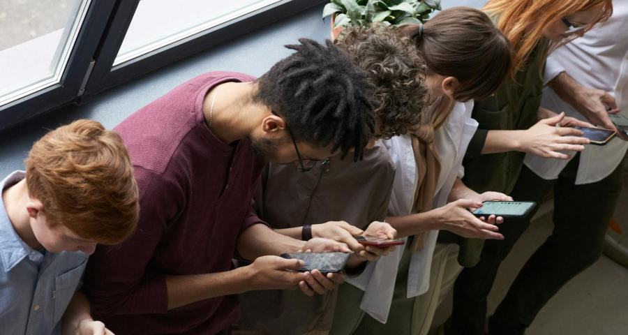 Looking down at a row of young adults all looking at their phones. By Fauxels on Pexels