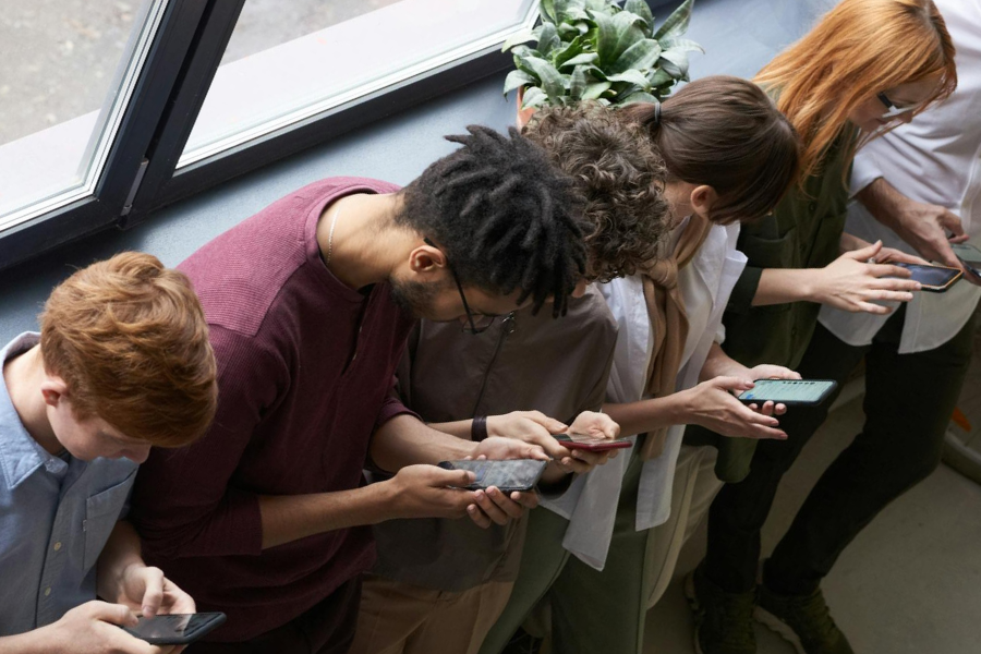 Looking down at a row of young adults all looking at their phones. By Fauxels on Pexels