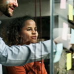A man and woman looking at sticky notes on a glass wall