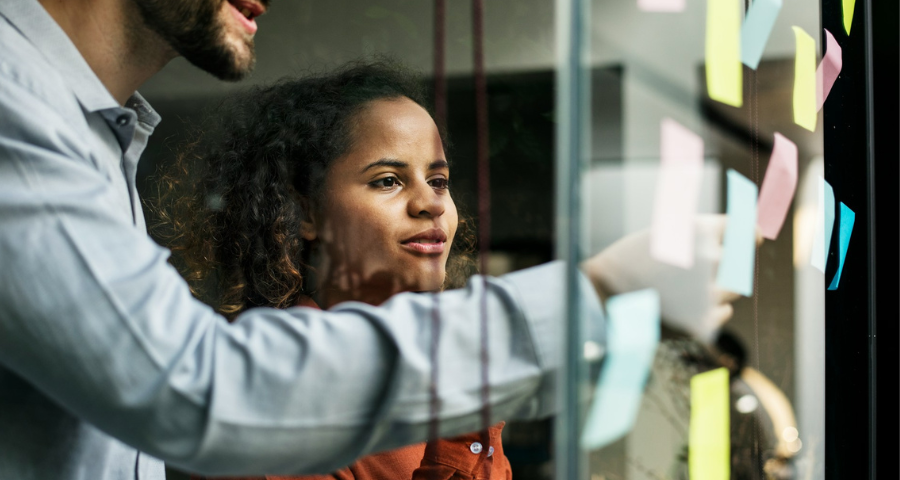 A man and woman looking at sticky notes on a glass wall