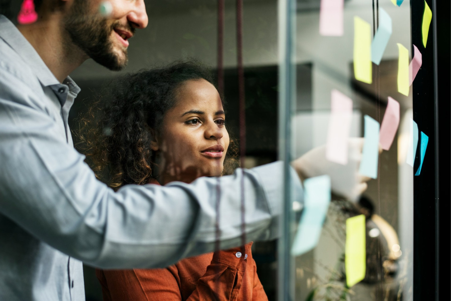 A man and woman looking at sticky notes on a glass wall