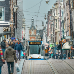 A street scene in the Netherlands with people, a tram and shops