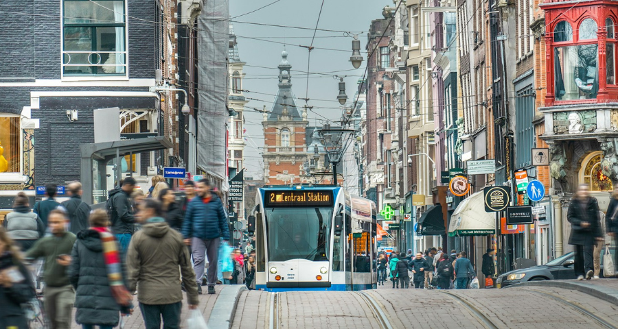 A street scene in the Netherlands with people, a tram and shops
