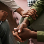 A woman's hand on the arm of a man as they sit close together - depicting listening and empathy. By Getty Images for Unsplash+