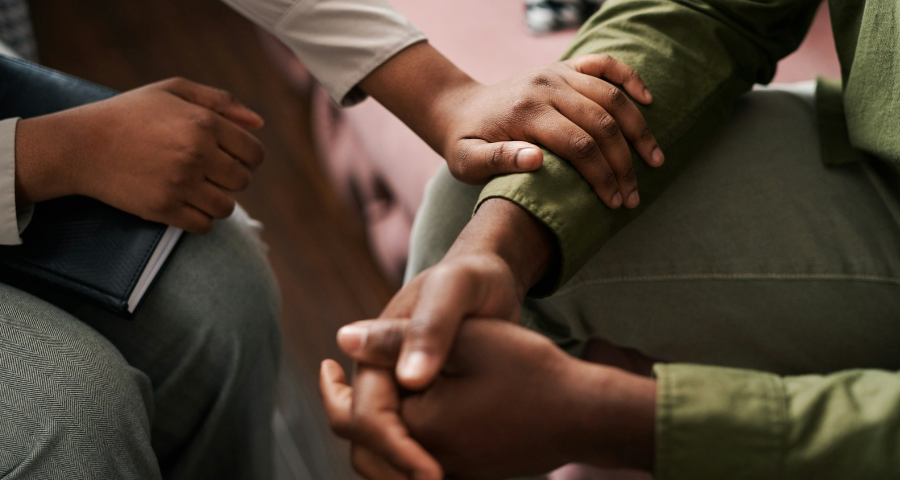 A woman's hand on the arm of a man as they sit close together - depicting listening and empathy. By Getty Images for Unsplash+