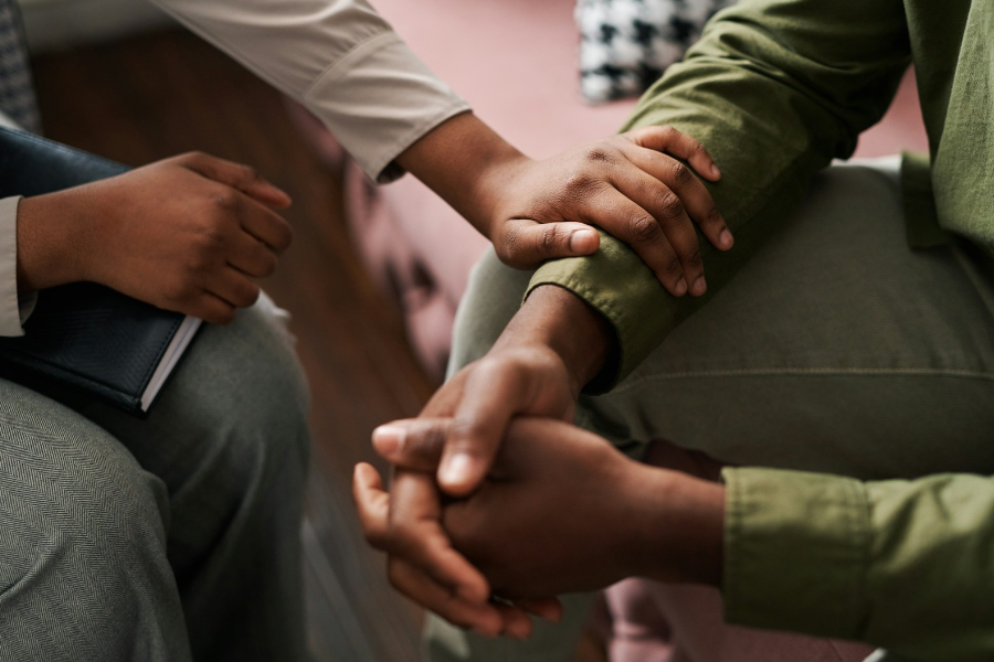A woman's hand on the arm of a man as they sit close together - depicting listening and empathy. By Getty Images for Unsplash+