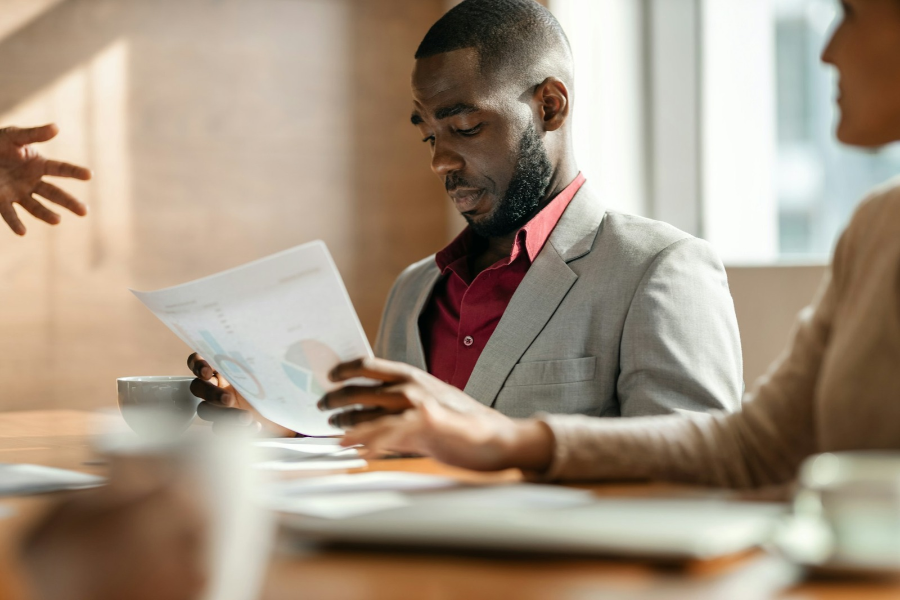 Black man in a suit, sitting at a table in a meeting, looking down at data on sheets of papers_getty Images unsplash+